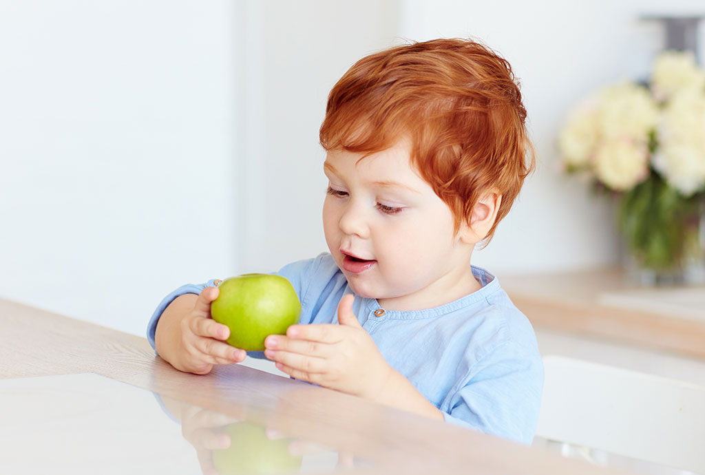 Junge schaut einen grünen Apfel an